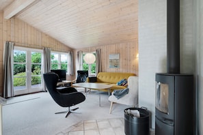 Ein modernes Wohnzimmer mit Sofa, Sessel und Tisch, einem Kamin und großen Fenstern mit Vorhängen.