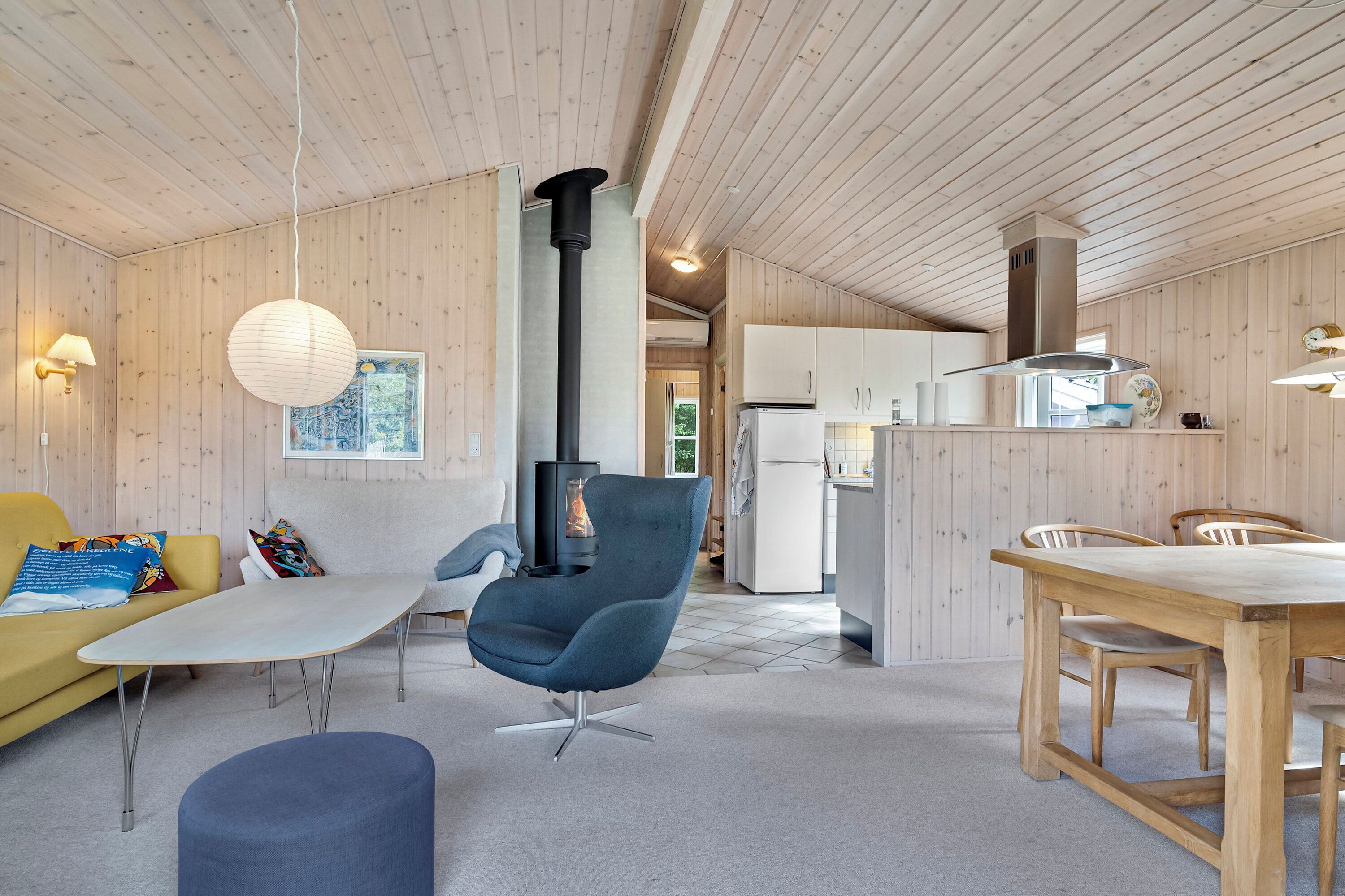 A modern interior with a wooden ceiling, a sofa, a chair, a dining table, and a kitchen area.