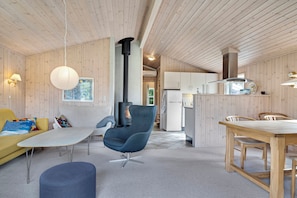 Ein modernes Interieur mit Holzboden, einer Couch, einem Sessel, einem Esstisch und einer Küchenzeile.