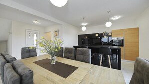 A modern kitchen with black appliances, a dining area with a wooden table and grey upholstered chairs, and a vase with yellow flowers on the table. - Awesome home in Nin with sauna (Nin)