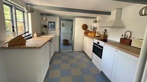 Une cuisine avec un carrelage à motifs, des placards blancs, un plan de travail en bois et une vue sur l’extérieur grâce à une porte ouverte.