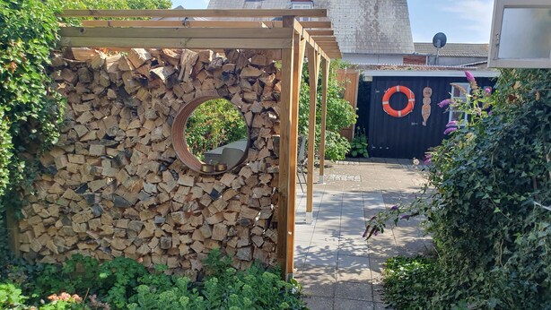 Un espace jardin agrémenté d’une pergola en bois, d’un miroir rond et d’une pile de bois de chauffage.