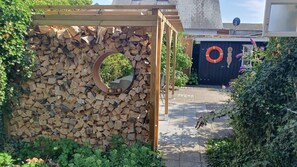 Een tuin met een houten pergola, een ronde spiegel en een stapel houtblokken.