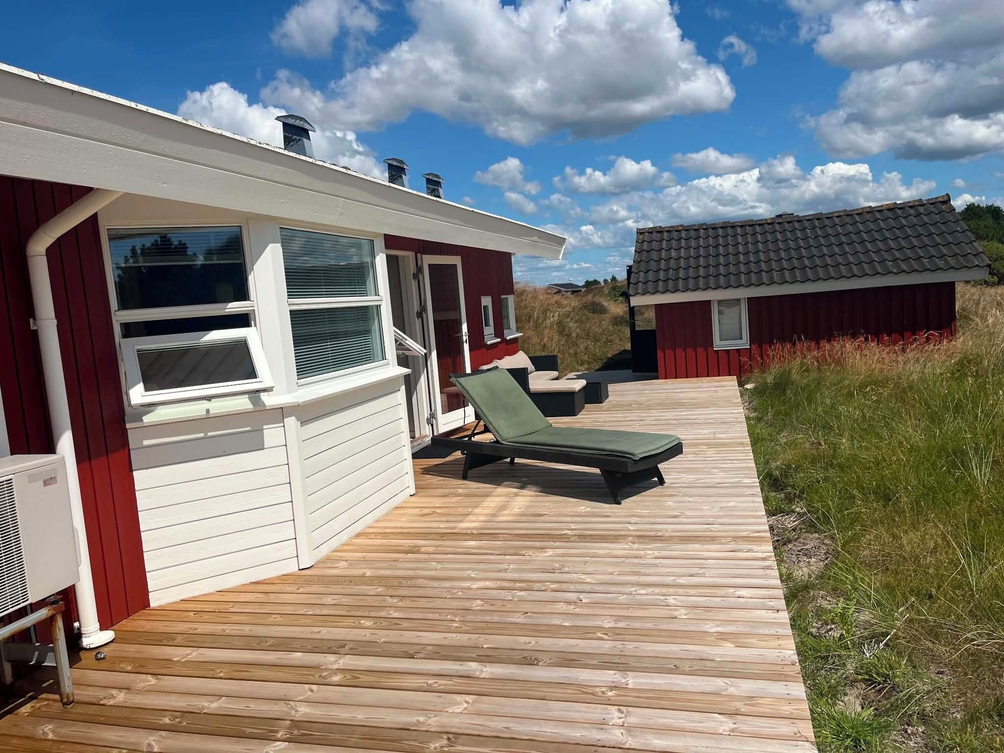 En træterrasse med en rød bygning, en lille tilbygning og en klar himmel.