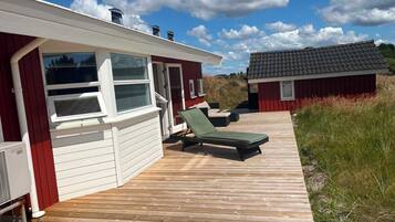 En træterrasse med en rød bygning, en lille tilbygning og en klar himmel.
