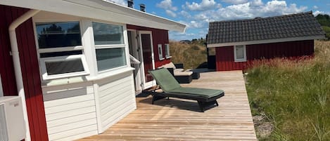 Une terrasse en bois, un bâtiment rouge, une petite construction adjacente et un ciel dégagé.
