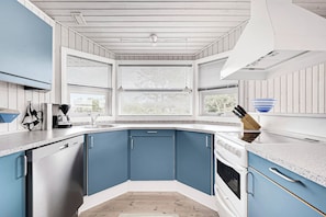 A kitchen with blue cabinets, a dishwasher, an oven, and a window with blinds. - Holiday house on Fanø near the sea (Fanø)