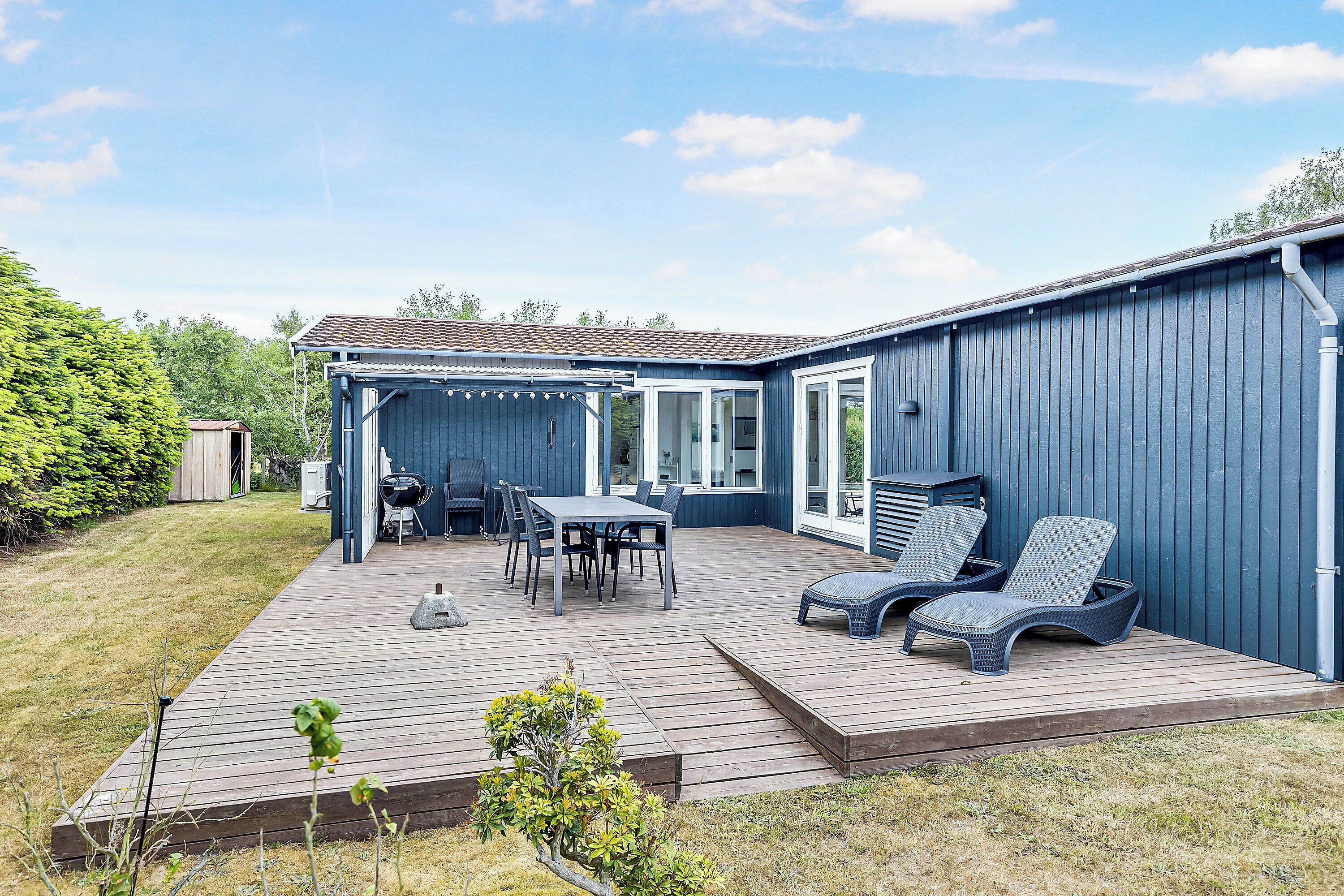 Eine Terrasse mit Tisch und Stühlen, einem Grill und Liegestühlen.