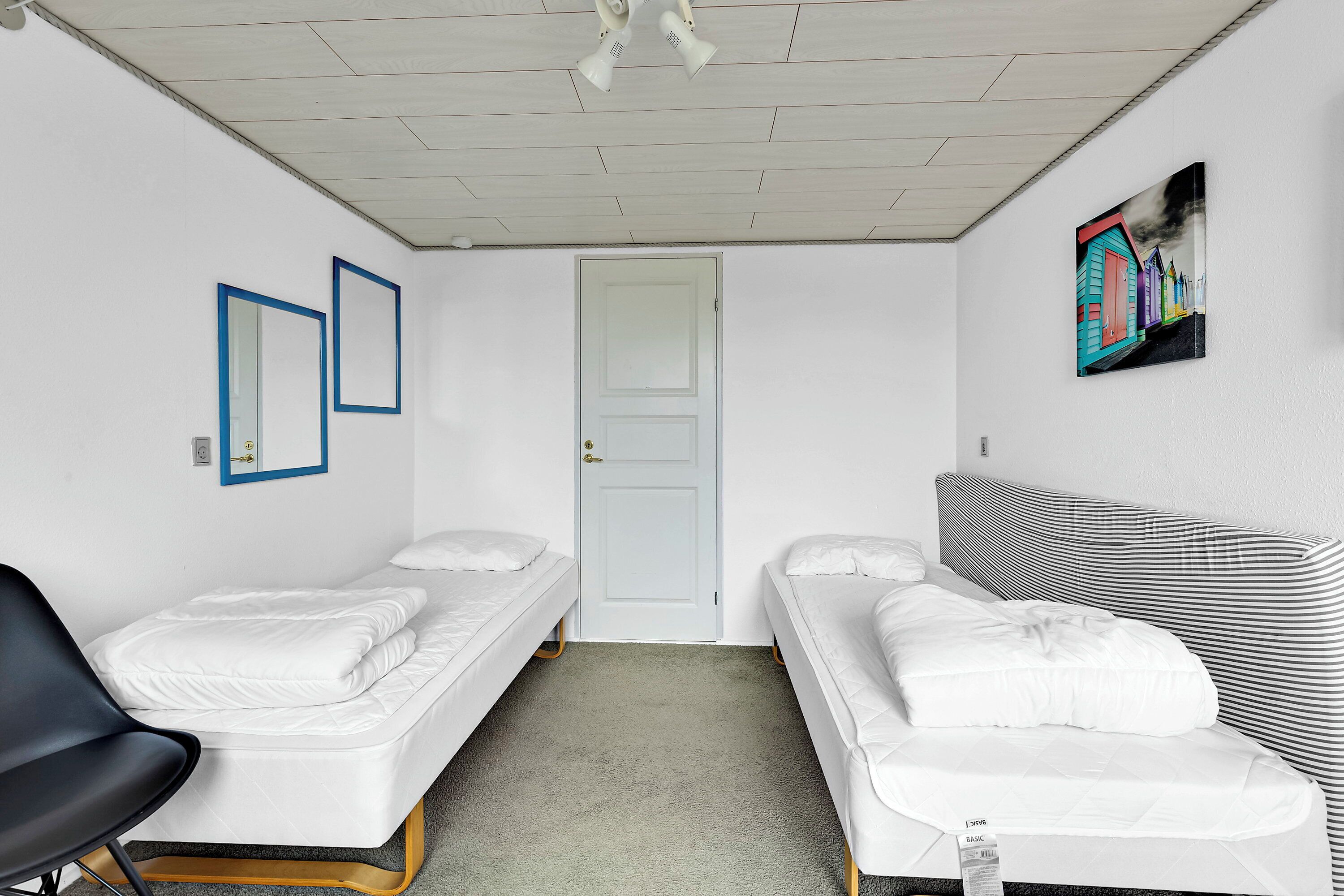 Une chambre avec deux lits simples, un canapé, une chaise, une porte et un tableau encadré au mur.