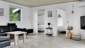 Ein modernes Wohnzimmer mit einem schwarzen Ledersofa, einem Holztisch, einem weißen Sessel und einem Fernseher.
