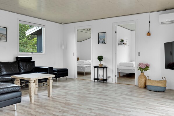Ein modernes Wohnzimmer mit einem schwarzen Ledersofa, einem Holztisch, einem weißen Sessel und einem Fernseher.