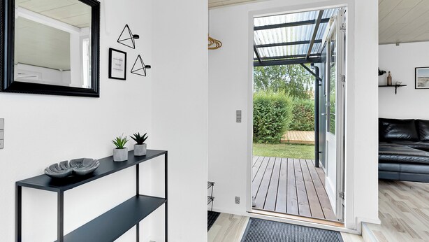 Ein modernes Interieur mit einem schwarzen Konsolentisch, einem Spiegel und einer Tür zu einer hölzernen Außenterrasse.