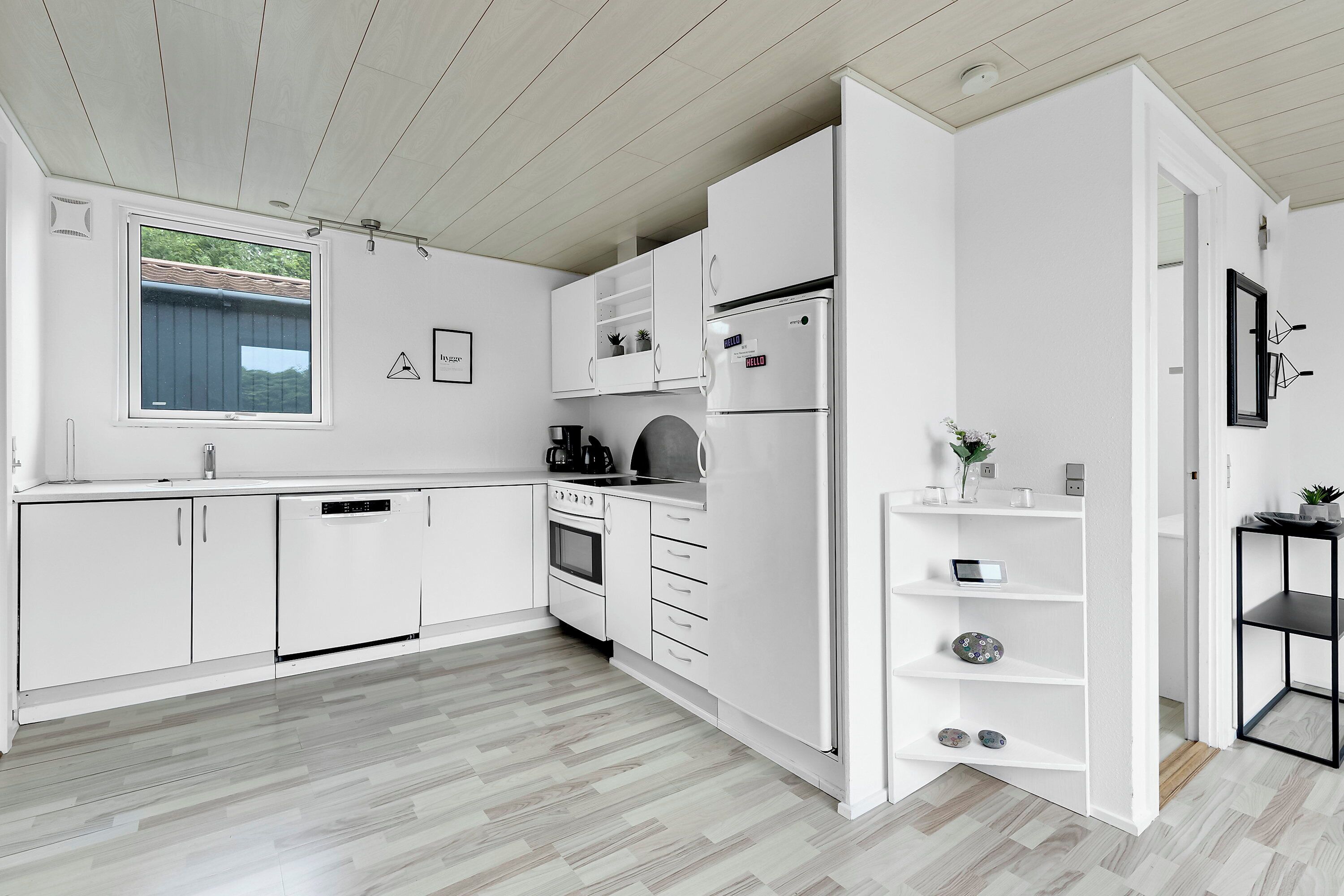 Une cuisine moderne avec des meubles blancs, un four encastré et une fenêtre donnant sur un espace verdoyant.