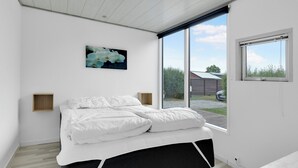 Ein Schlafzimmer mit einem Bett, einem Bild, einem Fenster und Blick ins Freie.