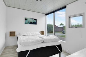 Ein Schlafzimmer mit einem Bett, einem Bild, einem Fenster und Blick ins Freie.
