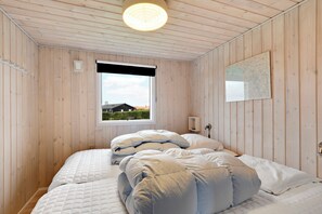 A room with wooden walls, a window with a view, a bed with white bedding, and a wall-mounted light fixture. - Fantastic view over Venø bay (Vinderup)