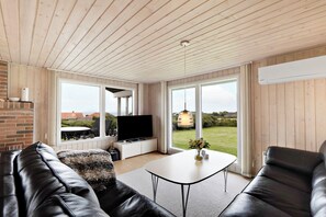 Een moderne woonkamer met een leren bank, een witte salontafel, een flatscreen televisie en grote ramen met uitzicht op het buitenlands gebied.
