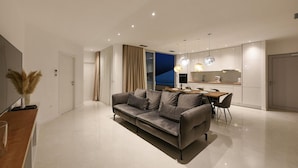 Een moderne woonkamer met een grijze bank, een eethoek met een houten tafel, en een keuken met witte kastjes.