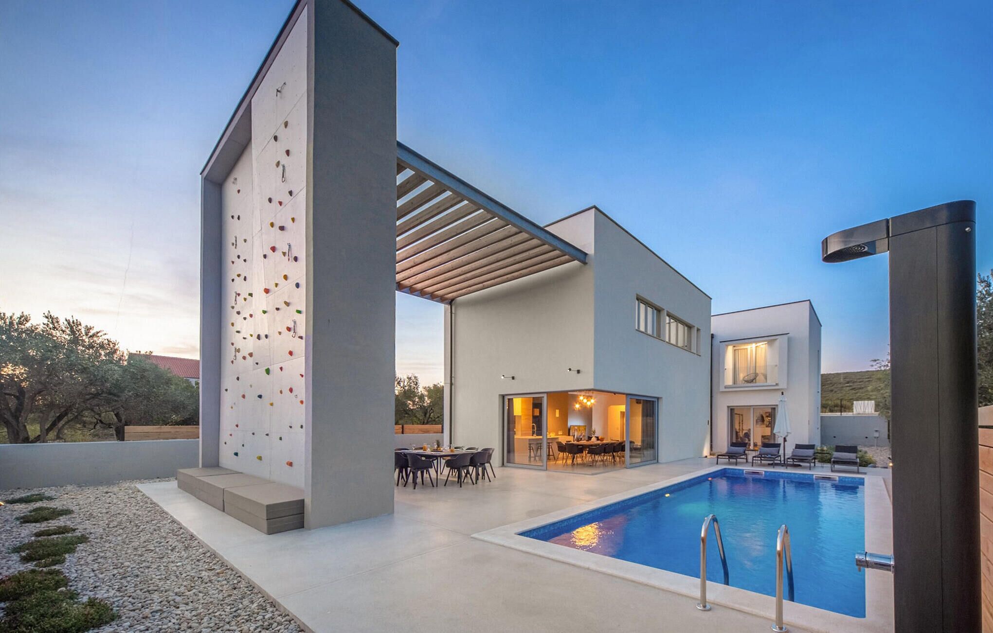 Una casa moderna con una pared de escalar, piscina y zona de patio.