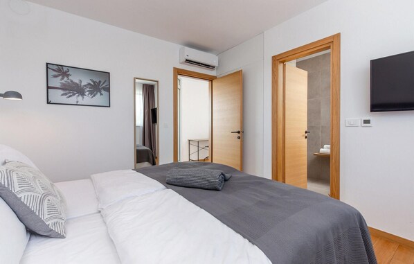 A bedroom with a bed, a TV, a picture on the wall, and a door leading to a bathroom.