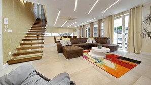 A modern living room with a staircase, a brown sectional sofa, a white coffee table, and a colorful rug. - Luxurious home in Zaton with sauna (Zaton)