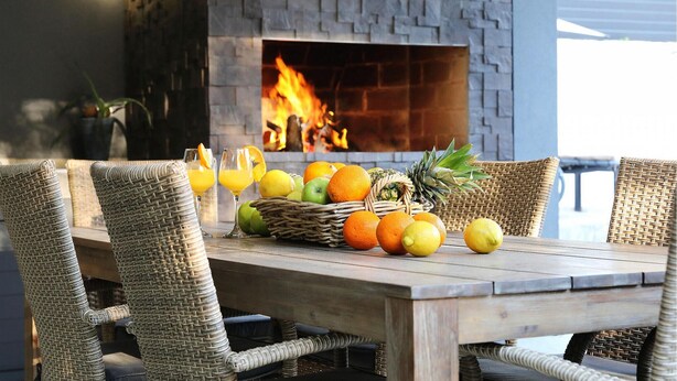 A wooden table with wicker chairs, a fruit basket, and glasses of orange juice in front of a stone fireplace with a fire. - Luxurious home in Zaton with sauna (Zaton)
