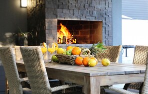 A wooden table with wicker chairs, a fruit basket, and glasses of orange juice in front of a stone fireplace with a fire. - Luxurious home in Zaton with sauna (Zaton)