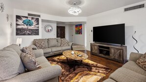 Ein Wohnzimmer mit einem großen Flachbildfernseher, grauen Sofas, einem Couchtisch und einem gemusterten Teppich.