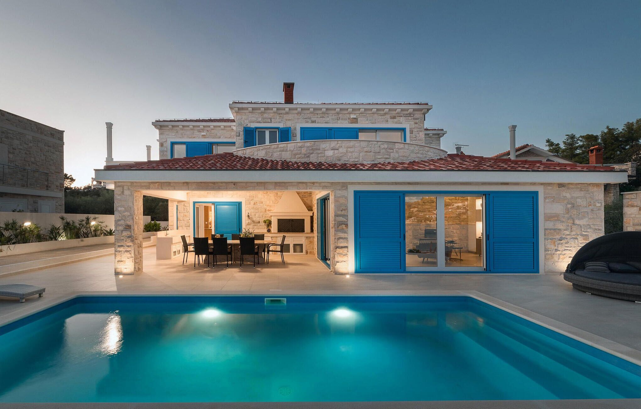 Una casa de dos pisos con piscina, destacando por su fachada de piedra y contraventanas azules.