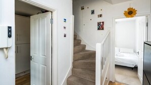 Un escalier menant à une chambre à coucher avec un lit, un mur blanc orné de tableaux et un motif décoratif représentant un soleil.