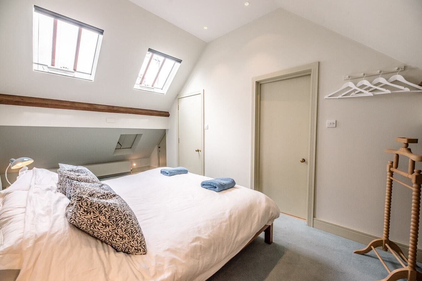 Une chambre à coucher comprenant un lit, deux fenêtres, une armoire et un porte-manteau en bois.