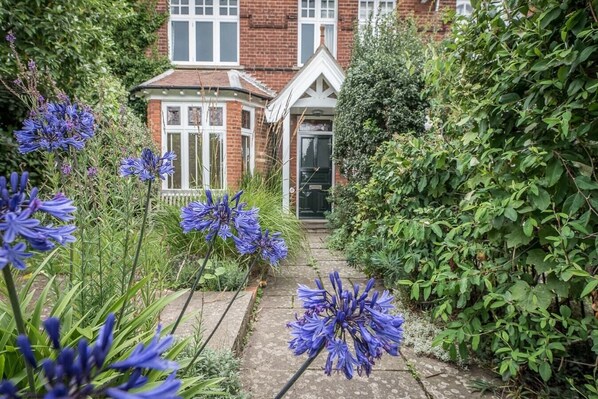 Stroll through the lush garden, lined with vibrant flowers and a variety of plants, to the traditional house with a brick facade and white-framed windows.