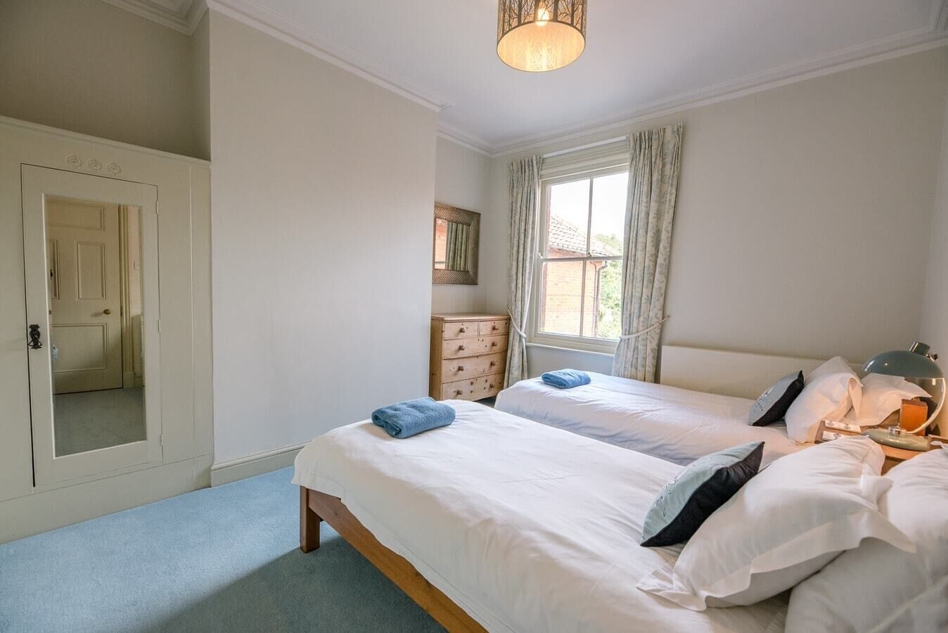 A bedroom with two beds, a dresser, a mirror, and a window with curtains.
