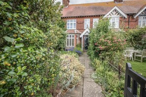 A garden pathway leading to a traditional brick house with white-framed windows and a front door.