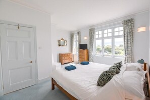 Relax in this serene bedroom with a large bed, dresser, and TV, offering a view of lush greenery.