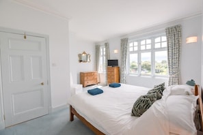 Relax in this serene bedroom with a large bed, dresser, and TV, offering a view of lush greenery.