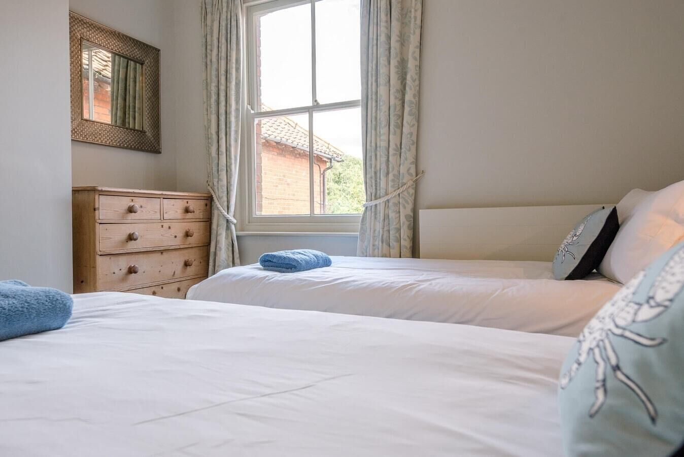 A bedroom with two beds, a wooden dresser, a window with curtains, and a mirror on the wall.