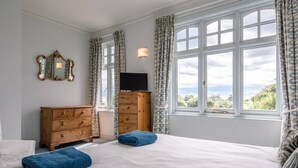 A bedroom with a large bed, a wooden dresser, a television, and a window with curtains. - 6 The Terrace, Walberswick (Walberswick)