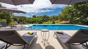 Zona de piscina con sillones reclinables, una mesita y sombrillas.