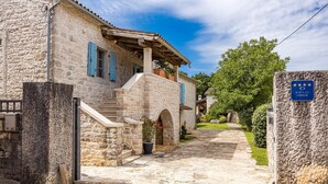 Edificio de piedra con una escalera que conduce a un porche cubierto, un cartel que indica que es un sitio protegido y un jardín bien cuidado.
