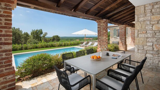 Patio esterno con piscina, tavolo e sedie, e vista sulla campagna.