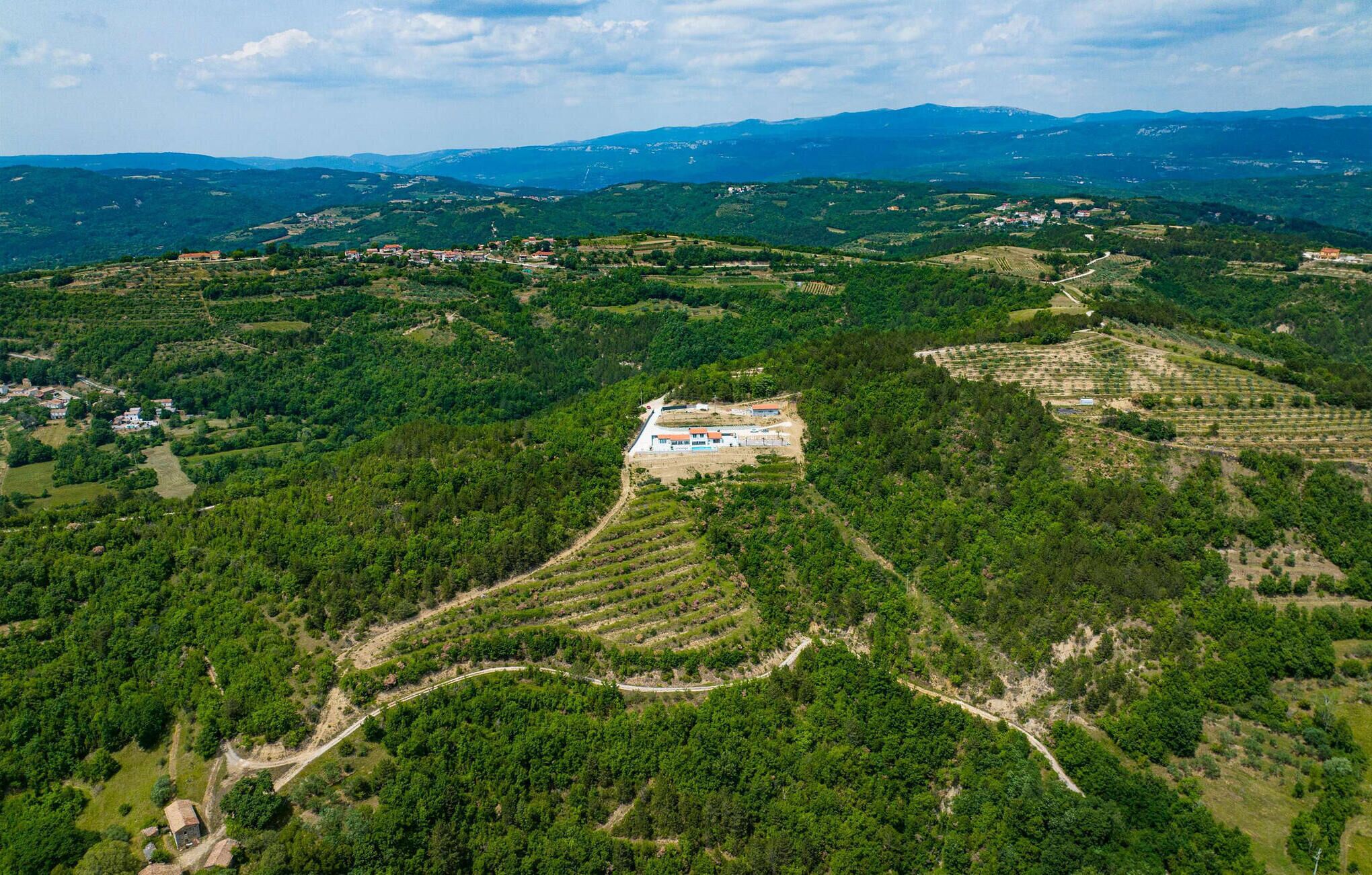 An aerial view of a rural landscape with terraced fields, a small cluster of buildings, and a winding road.