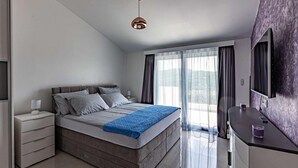 Un dormitorio moderno con una cama grande, una mesita de noche, una lámpara y vistas al exterior a través de un ventanal.