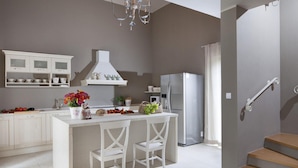 Een moderne keuken met witte kastjes, een centraal eiland met twee stoelen, een koelkast en een kroonluchter.