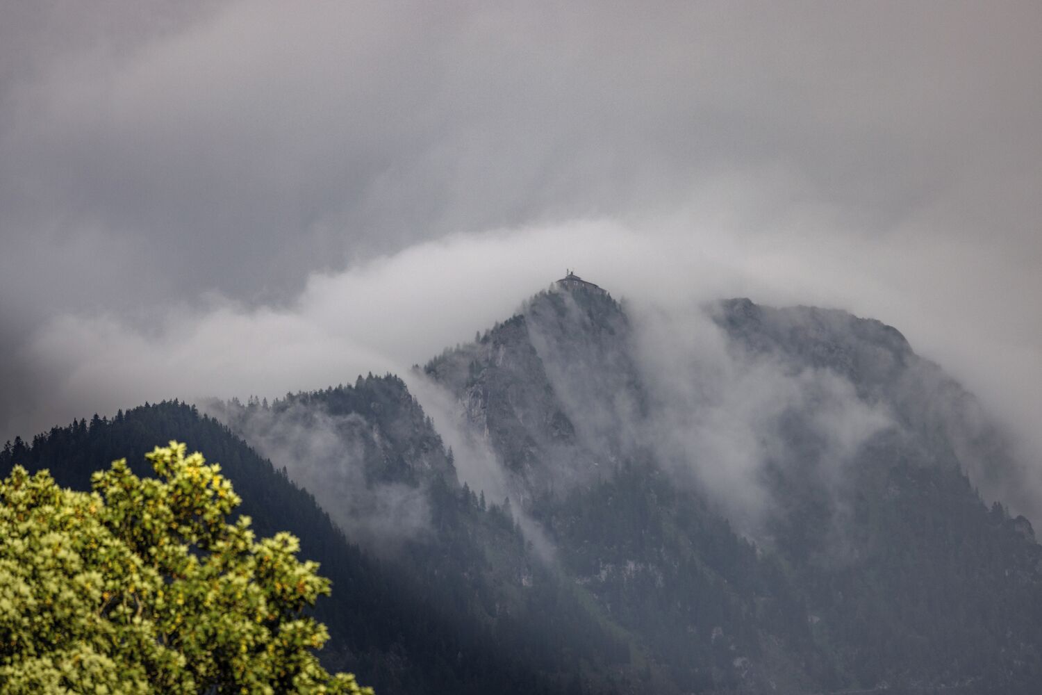 A mountain with a forested area and a building on top.
