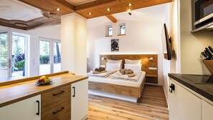 A modern bedroom with a wooden headboard, a bedside table with towels, and a view of a garden through large windows. - Appartment Reiter Alm 31 m² 1- 2 Pers., Wsz, Terrasse (Bischofswiesen)