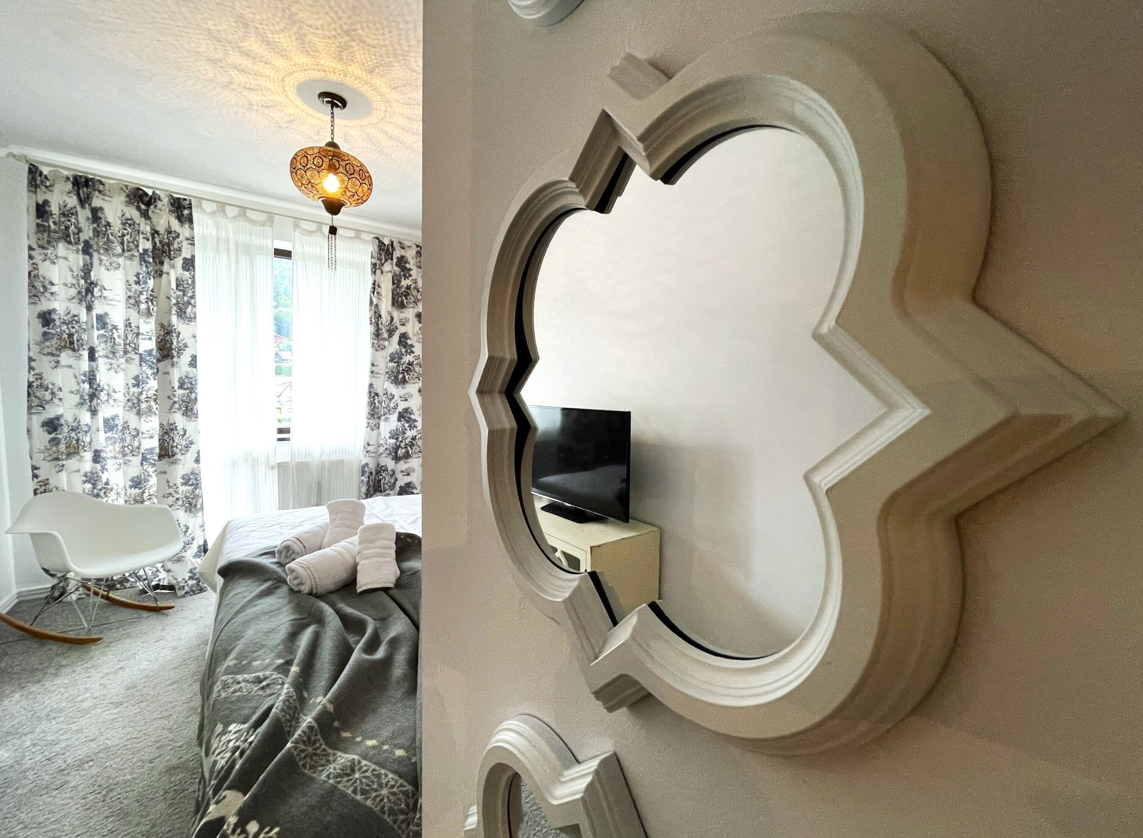 Ein Schlafzimmer mit einem Bett, einem Schaukelstuhl, einem an der Wand montierten Fernseher und einer dekorativen Deckenleuchte.