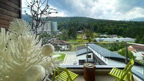 Un balcón con vistas a un pueblo, una planta decorativa y dos sillas verdes.