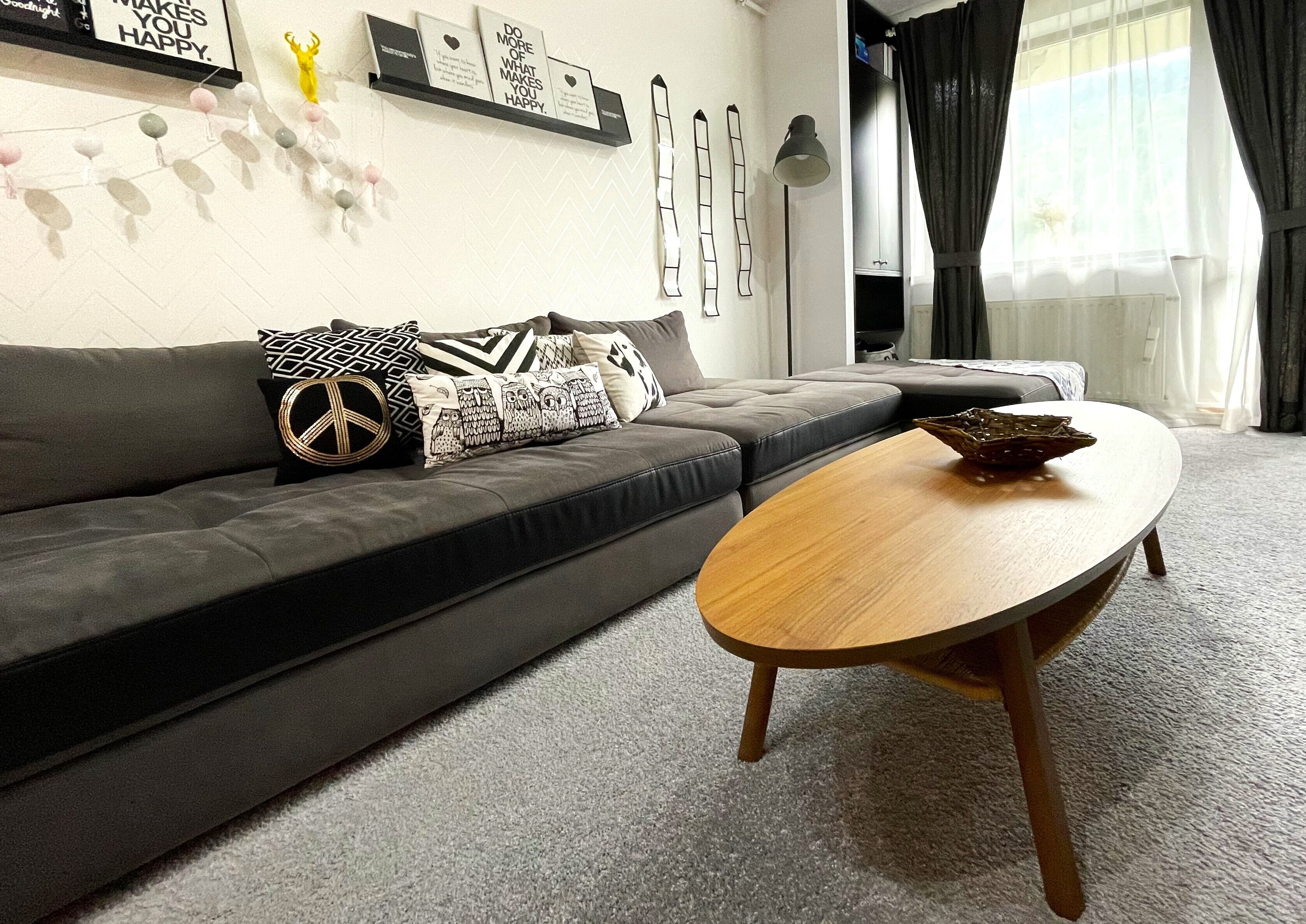 Un soggiorno moderno con un divano grigio, cuscini decorati, un tavolino in legno e decorazioni a parete tra cui citazioni motivazionali incorniciate e arte astratta.