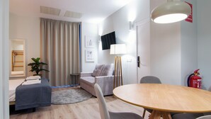 A modern hotel room with a bed, a sofa, a dining table, a TV, and a fire extinguisher. - VLC HOST - Reino 4 (Valencia)